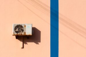 Rusty air conditioning unit casting shadow on a peach wall with blue stripe.
